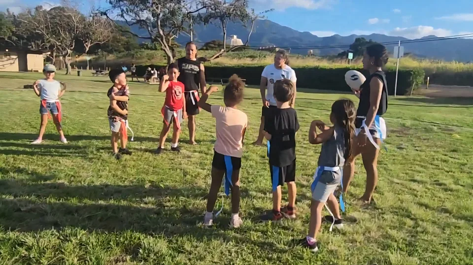 Young people and adults gathered on a grassy field during an outdoor movement activity.