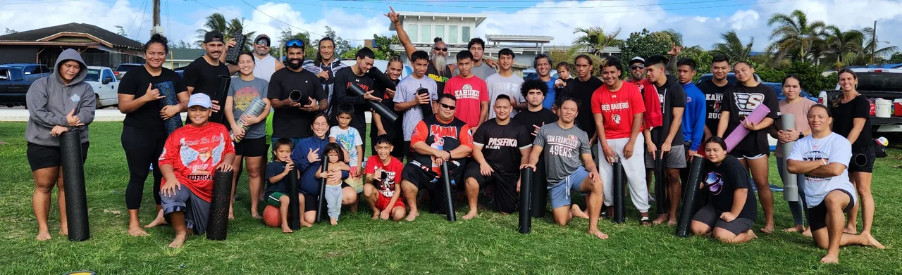 A multigenerational group standing together outdoors, many holding foam rollers.