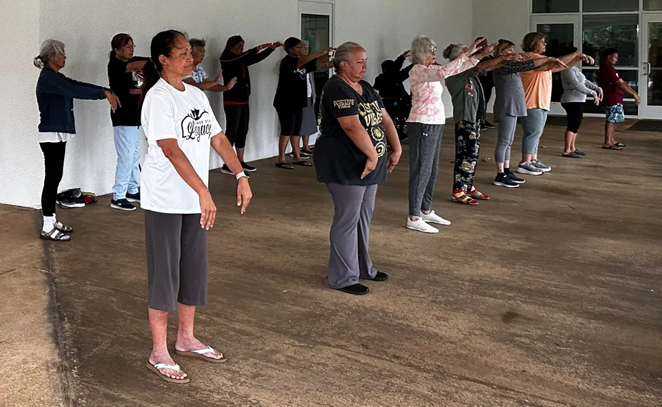 A group of kūpuna practicing Tai Chi together in a covered community space.