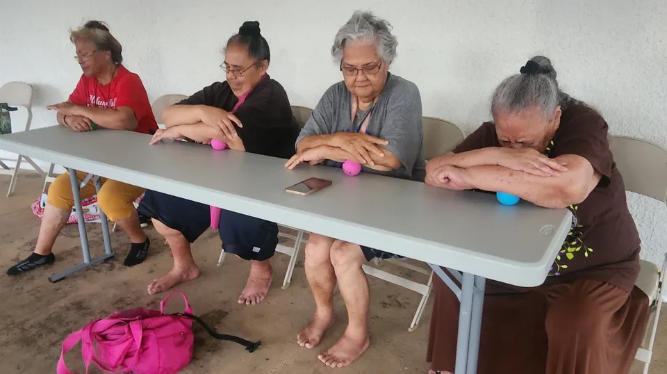 Four kūpuna seated at a table using small balls during a community movement session.