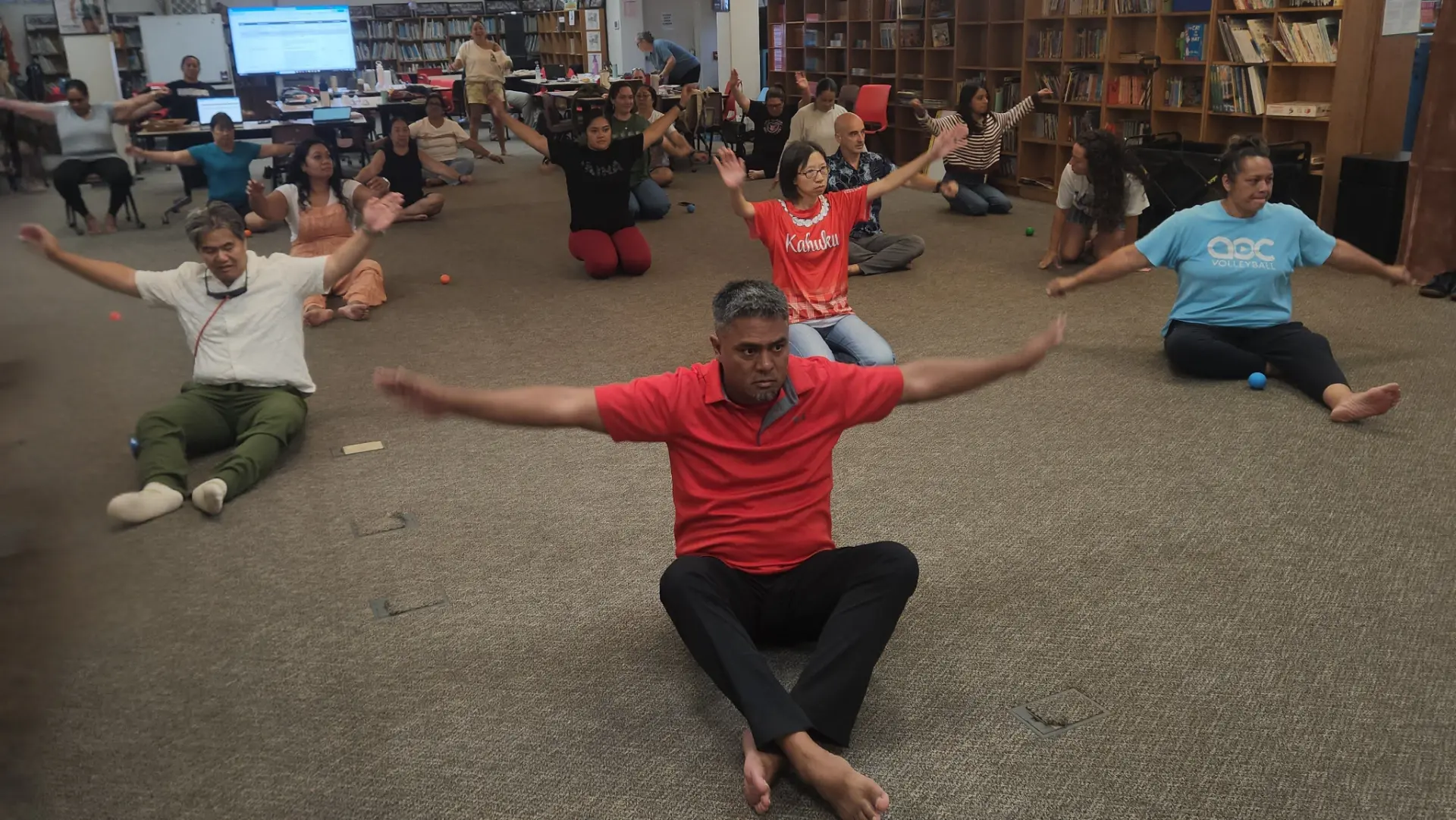 Elementary school staff participating in a seated movement-and-tension-release training in Koʻolauloa.